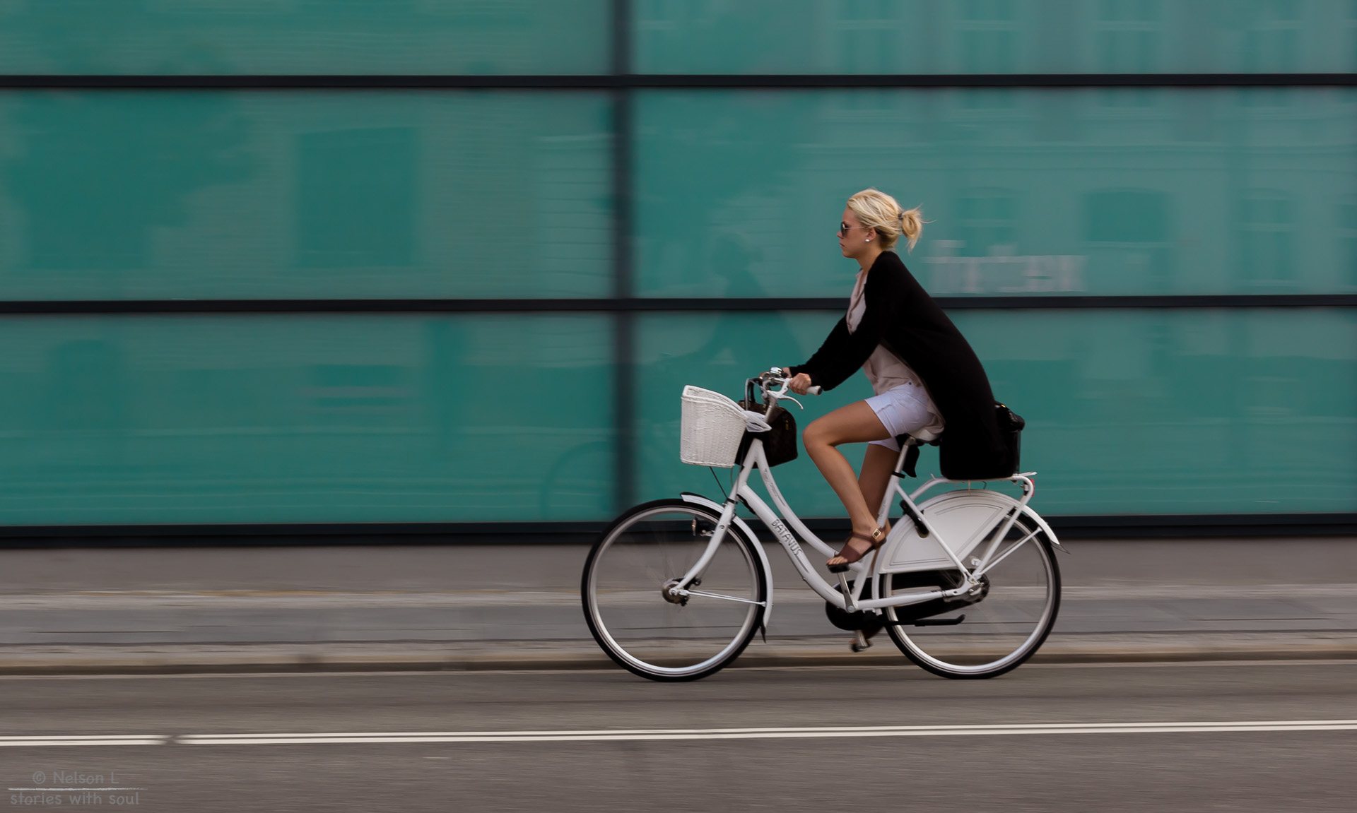 blond woman biking on white bicycle past big glass windows in city